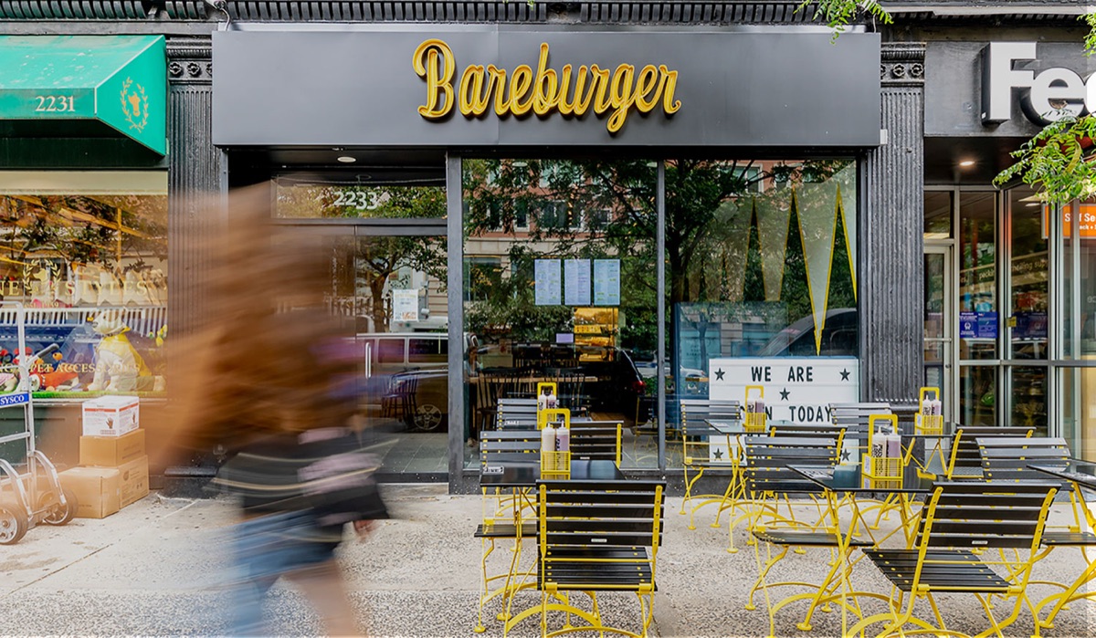 Bareburger storefront with gold script awning and yellow café seating
